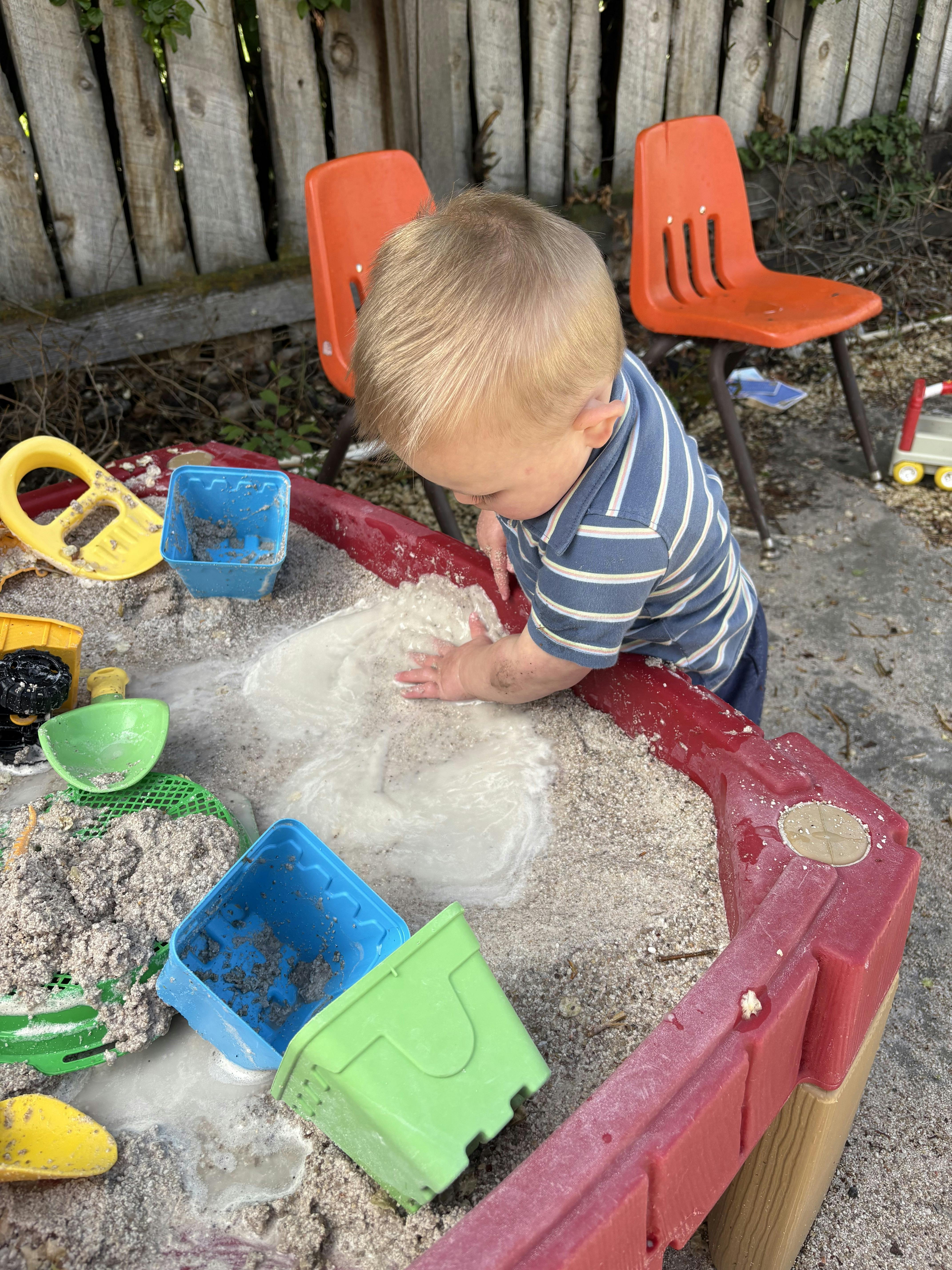 Child playing in a sandbox with wet sand and toys