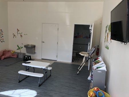 Room with a small white picnic table, high chair, and wall-mounted TV