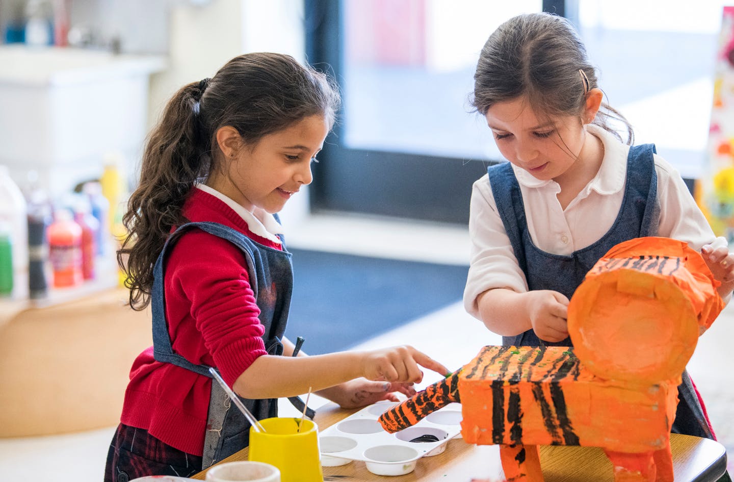 Two children painting a tiger sculpture in a classroom