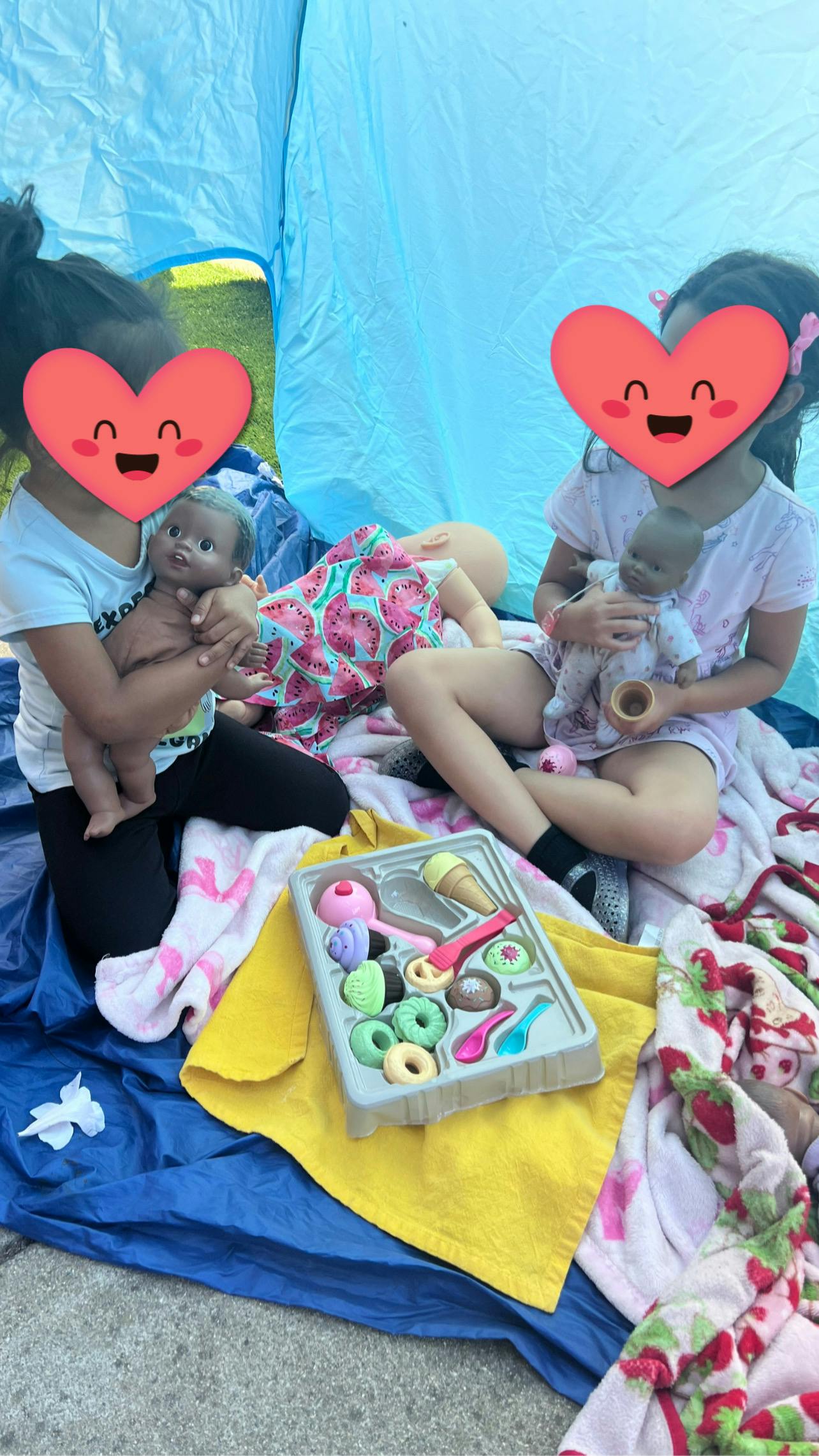 Two children sitting in a tent playing with dolls and toy food