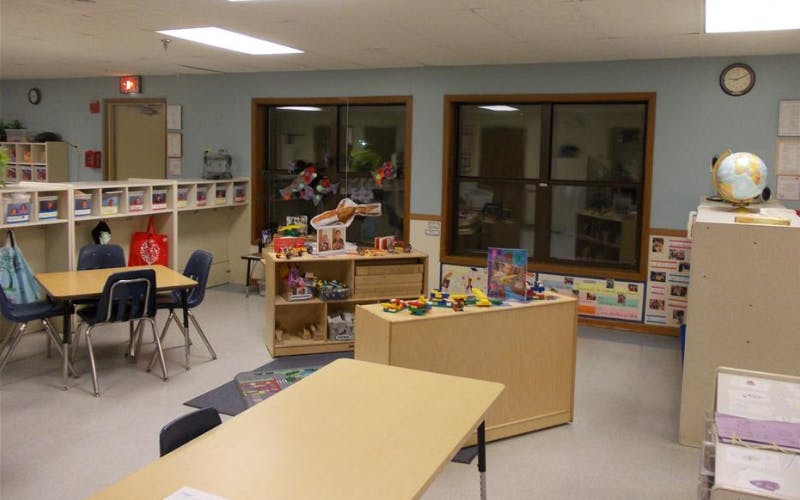 Classroom with tables, chairs, shelving units with cubbies, and windows