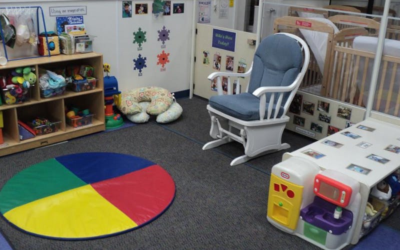 Classroom with child-sized furniture, cubbies with toys, a rocking chair, and cribs