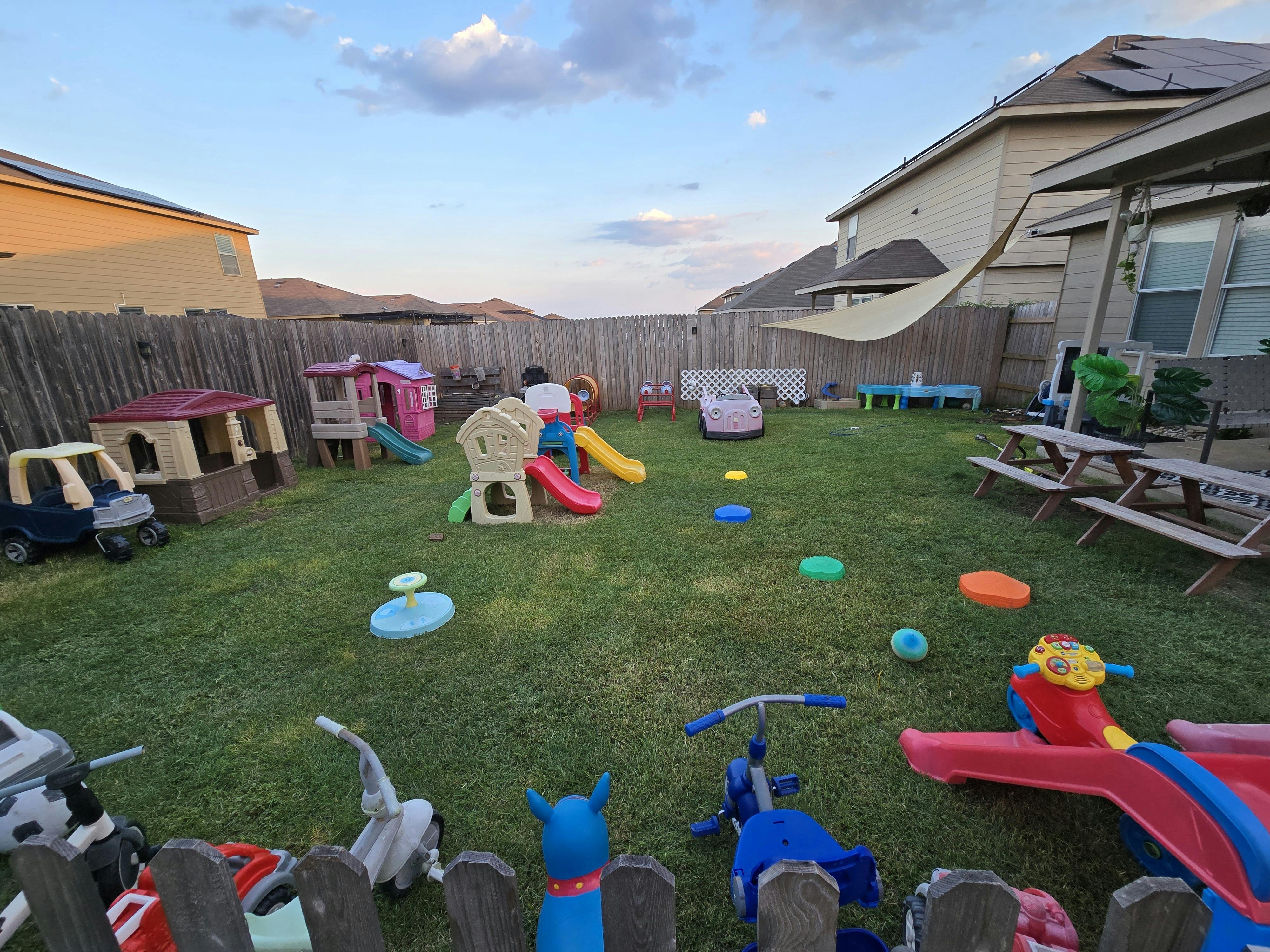 Backyard with various colorful children's play structures and toys on a grassy lawn