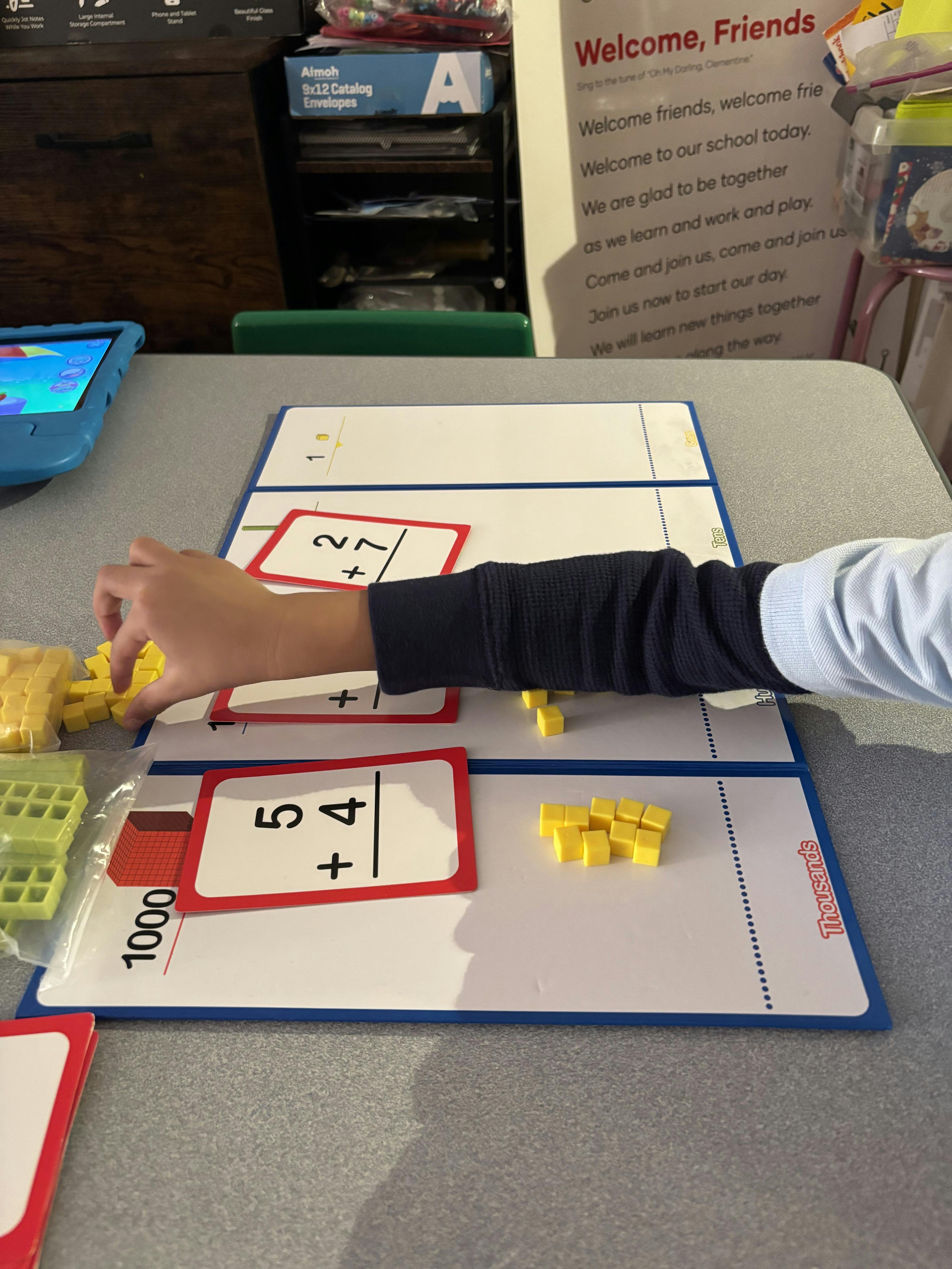Child's arm playing with yellow math cubes and addition cards on a desk