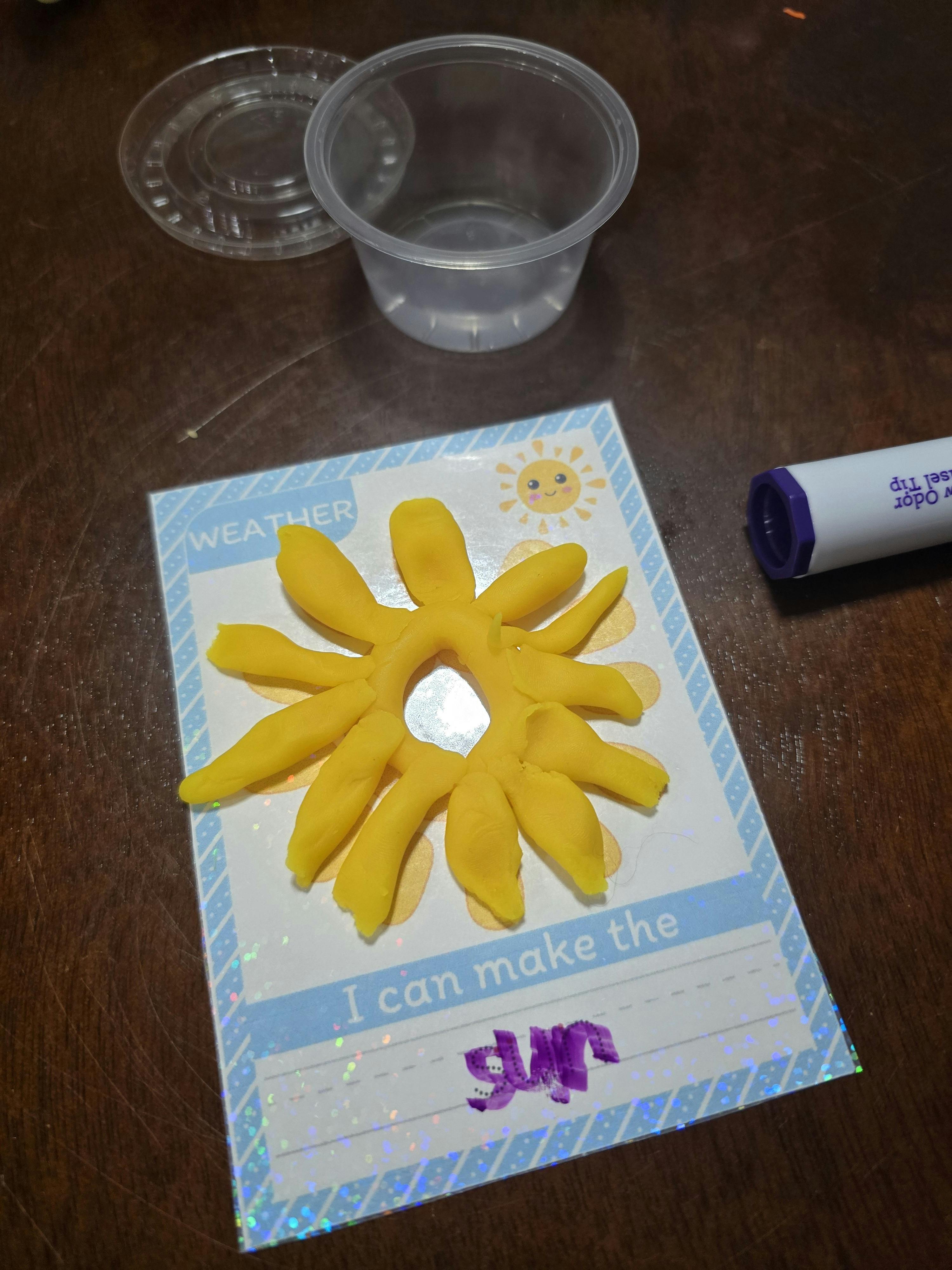 Yellow playdough sun on a card with a marker and plastic cups