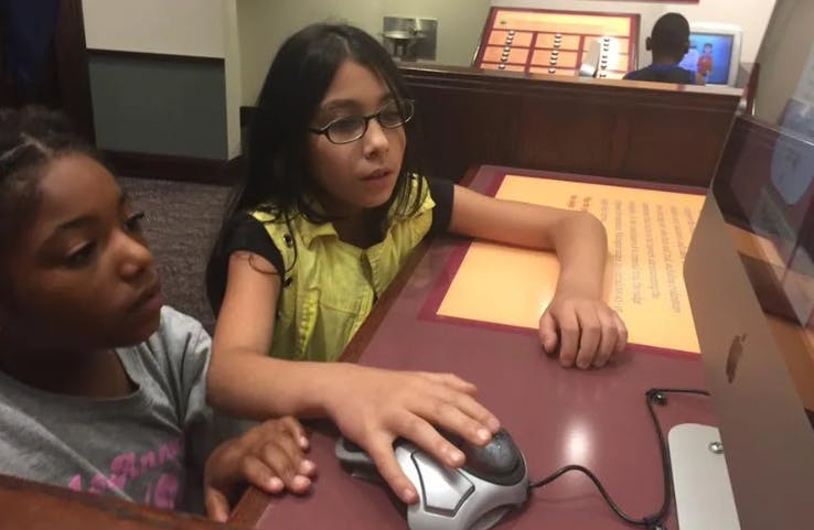 Two children looking at a computer screen, one child using a mouse