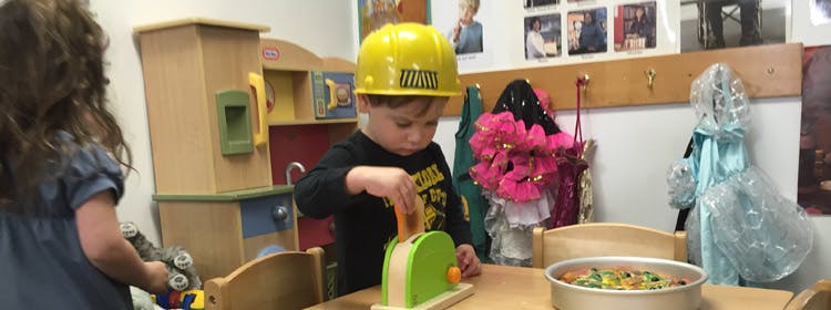 Child in a yellow hard hat playing with a toy toaster