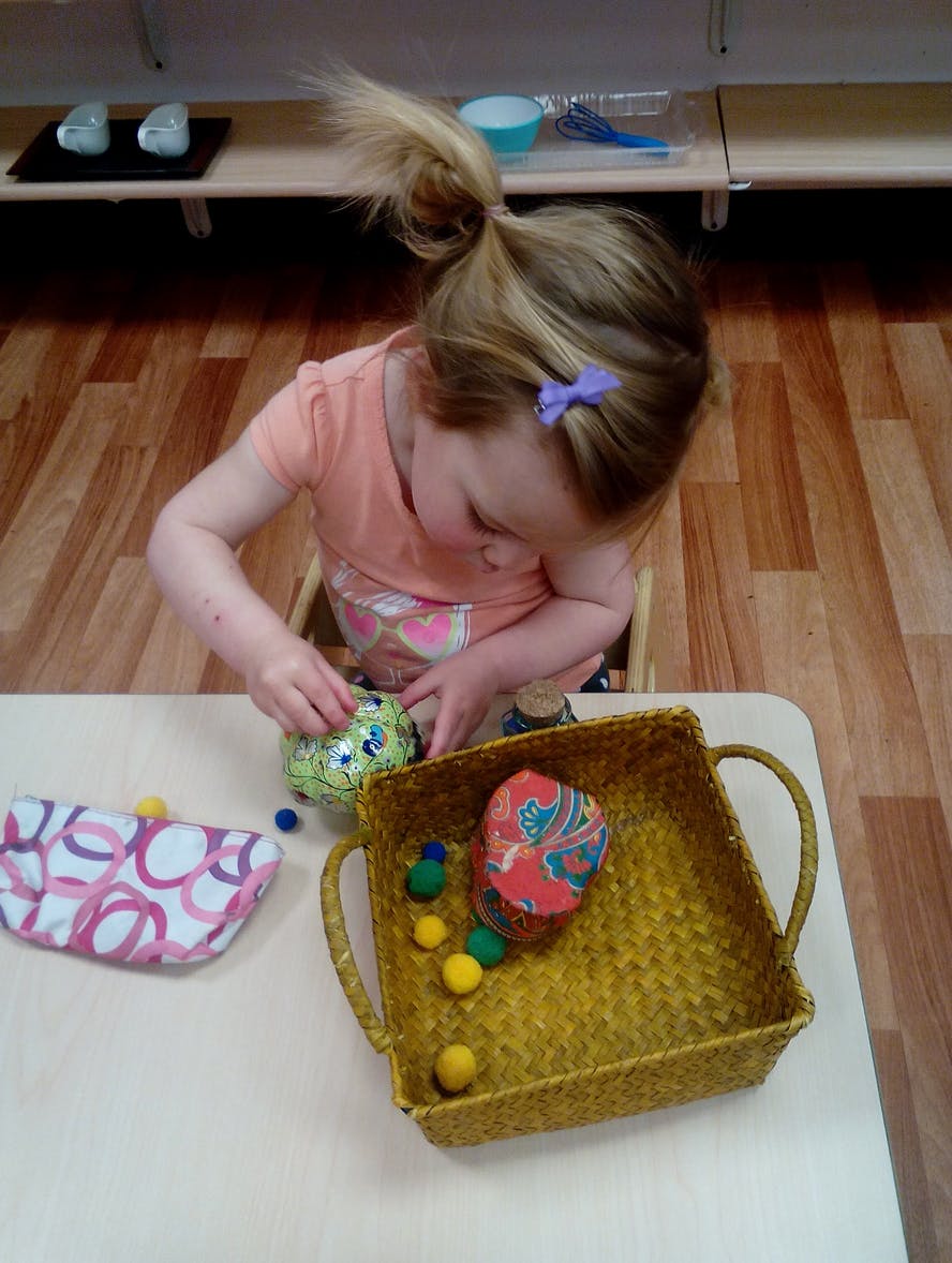 Child playing with small objects and a basket on a table