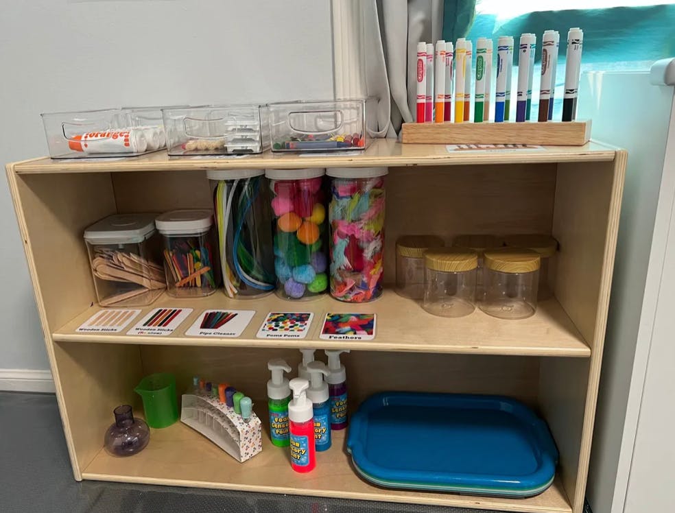 Wooden shelf with art supplies, including markers, jars, and bottles