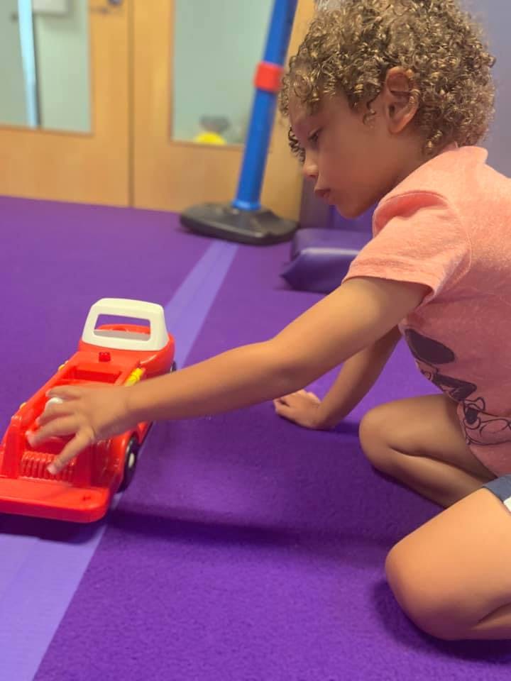 Child playing with a red toy car on a purple mat