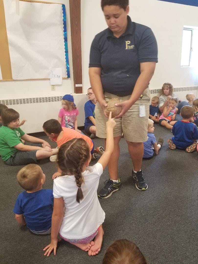 Person holding a ball with children sitting on the floor around them