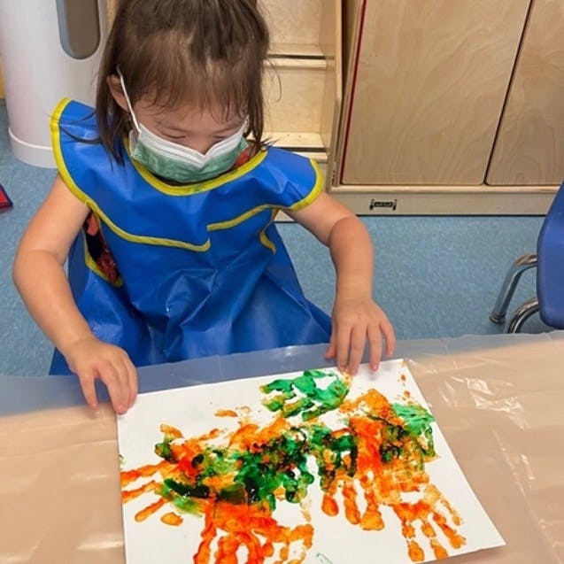 Child in a mask and smock making a handprint painting