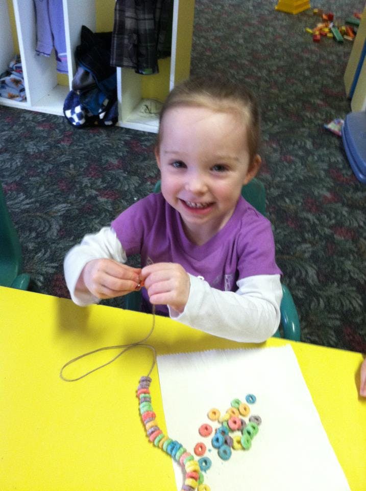 Child stringing colorful cereal pieces onto a necklace