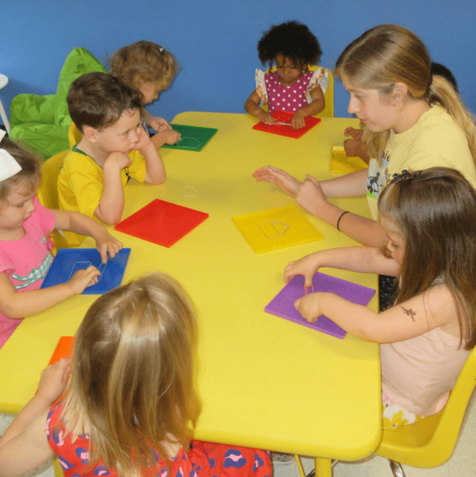 Children sitting around a yellow table with colorful papers