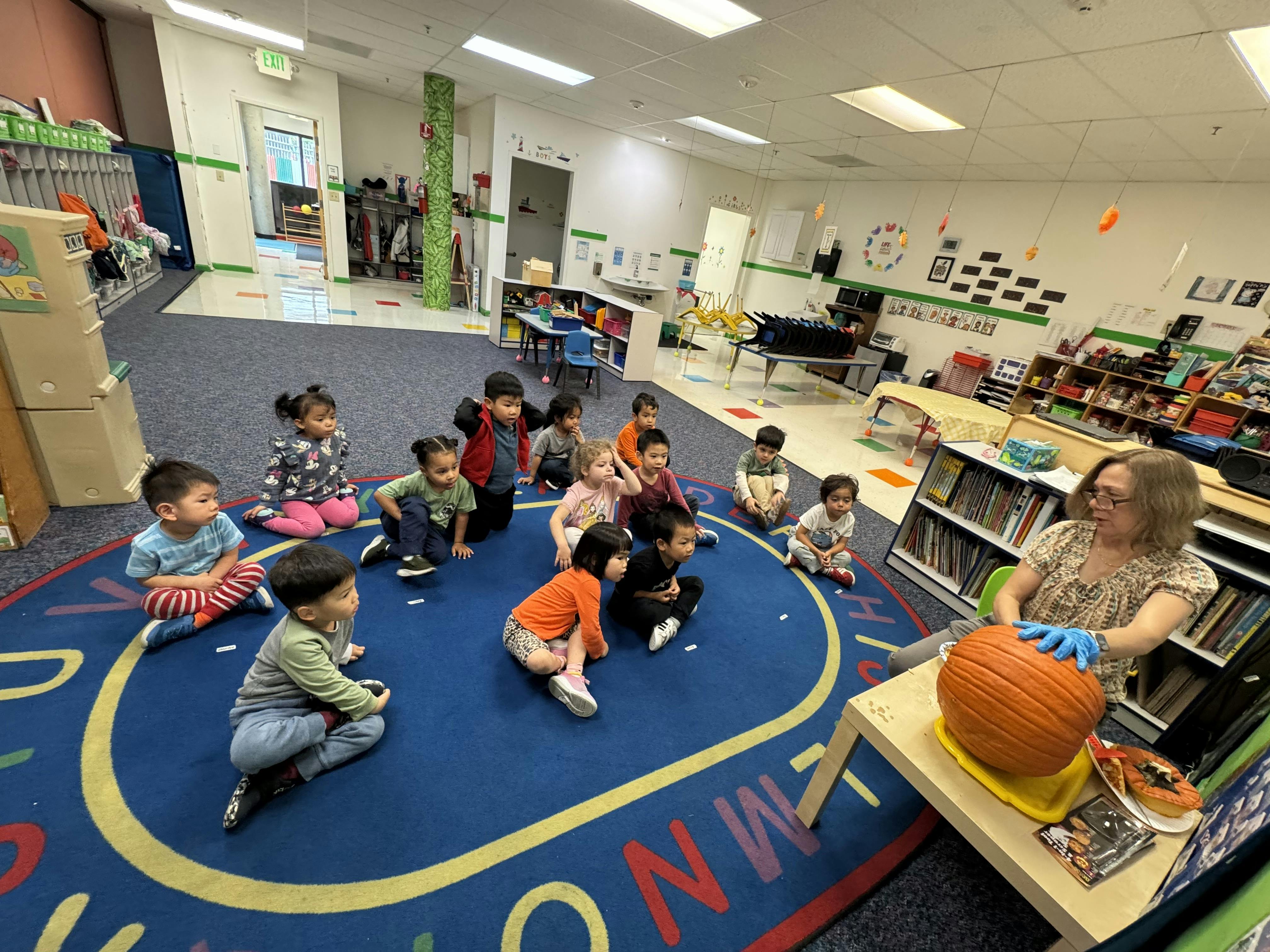 Adult with children in a classroom looking at a pumpkin