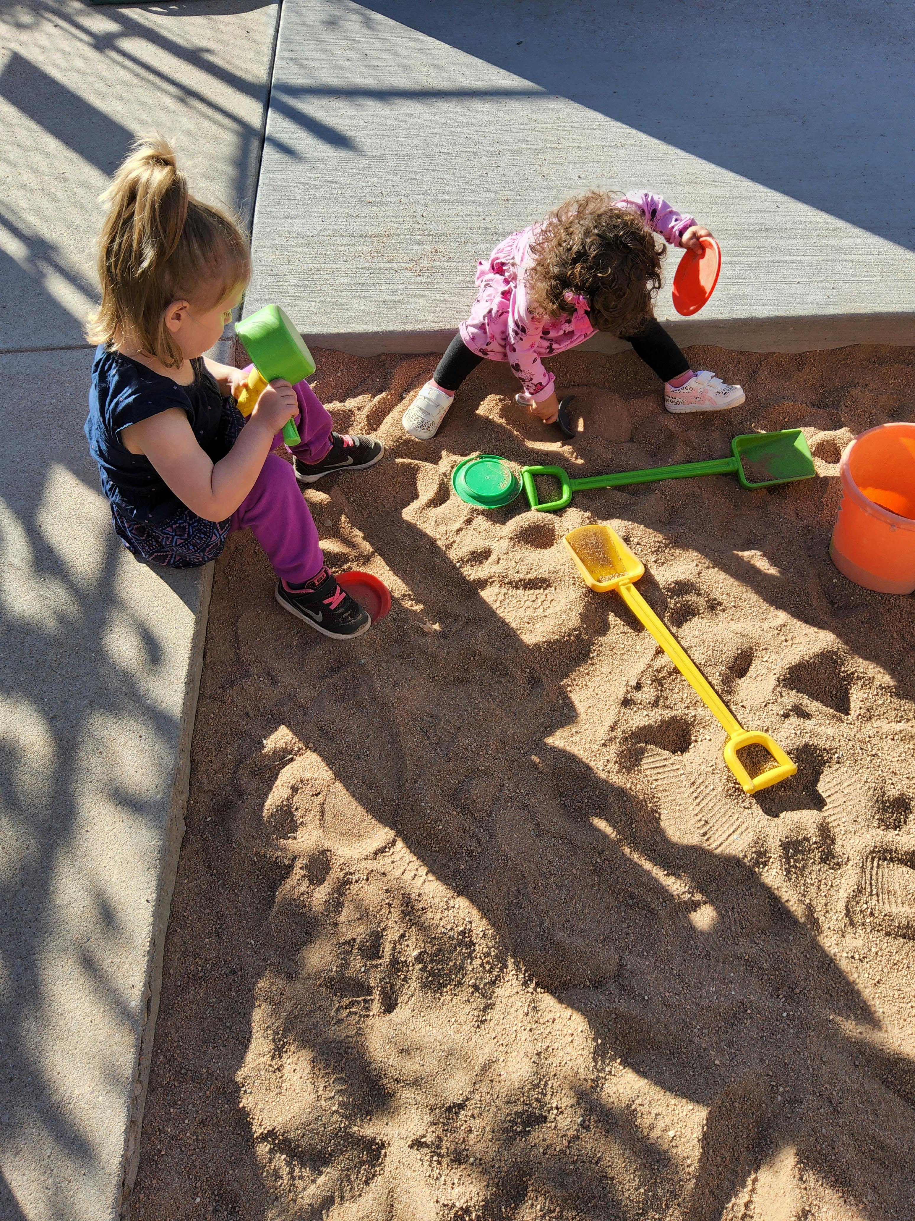 Two children playing in a sandbox with toys