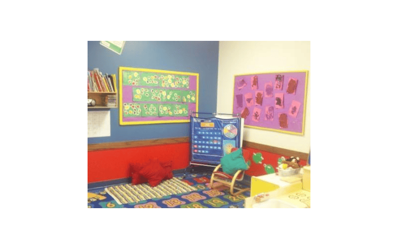 Children's classroom with artwork on bulletin boards, a calendar chart, and a rug
