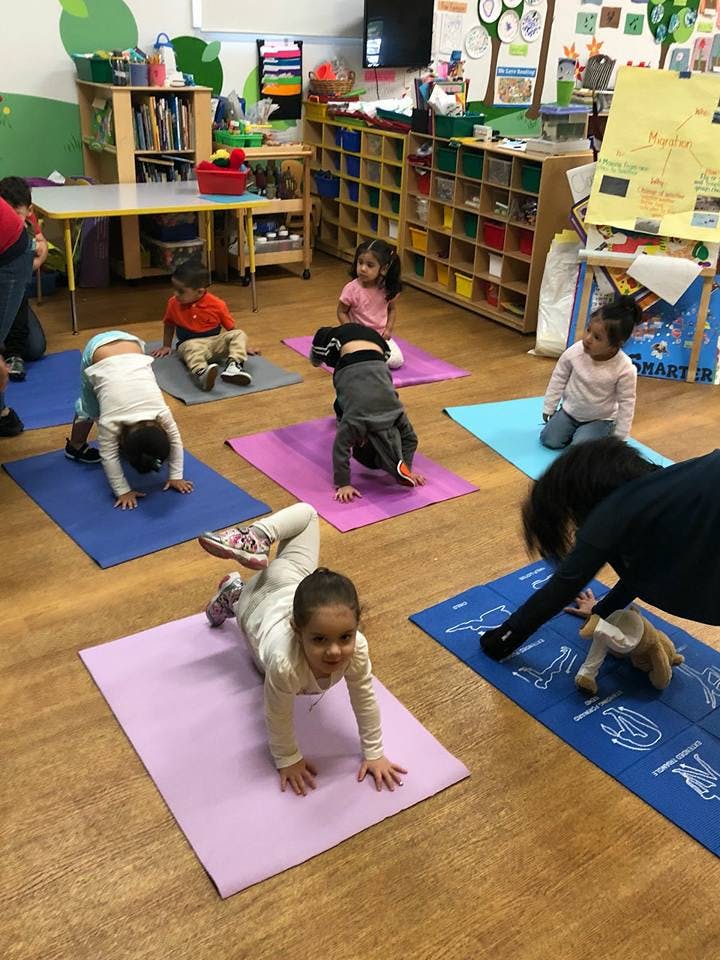 Children and an adult doing yoga poses on mats in a classroom