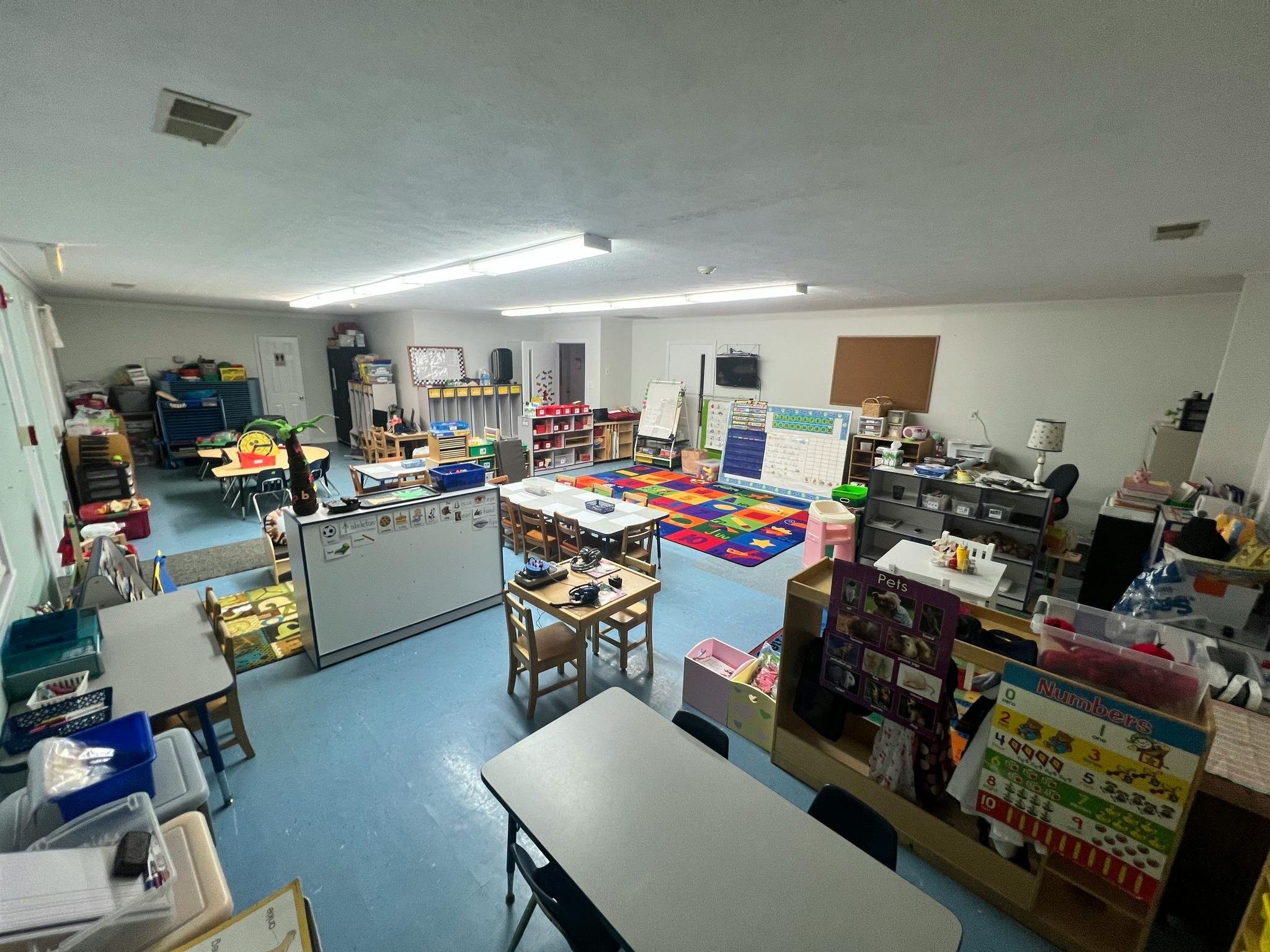Classroom with child-sized tables and chairs, learning rug, and educational materials