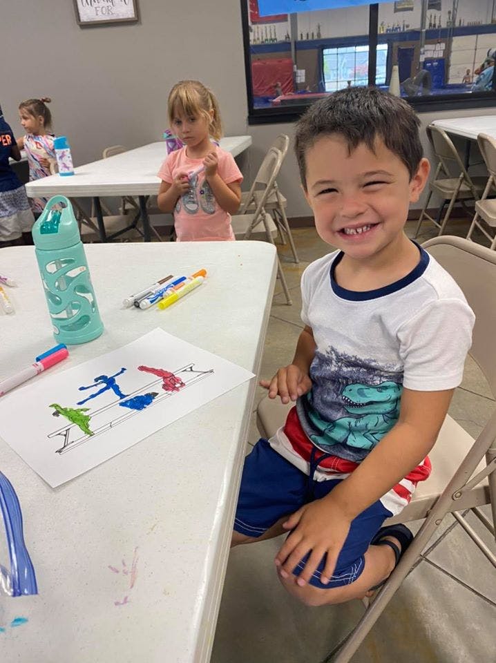 Child sitting at a table with a drawing, drawing and water bottle