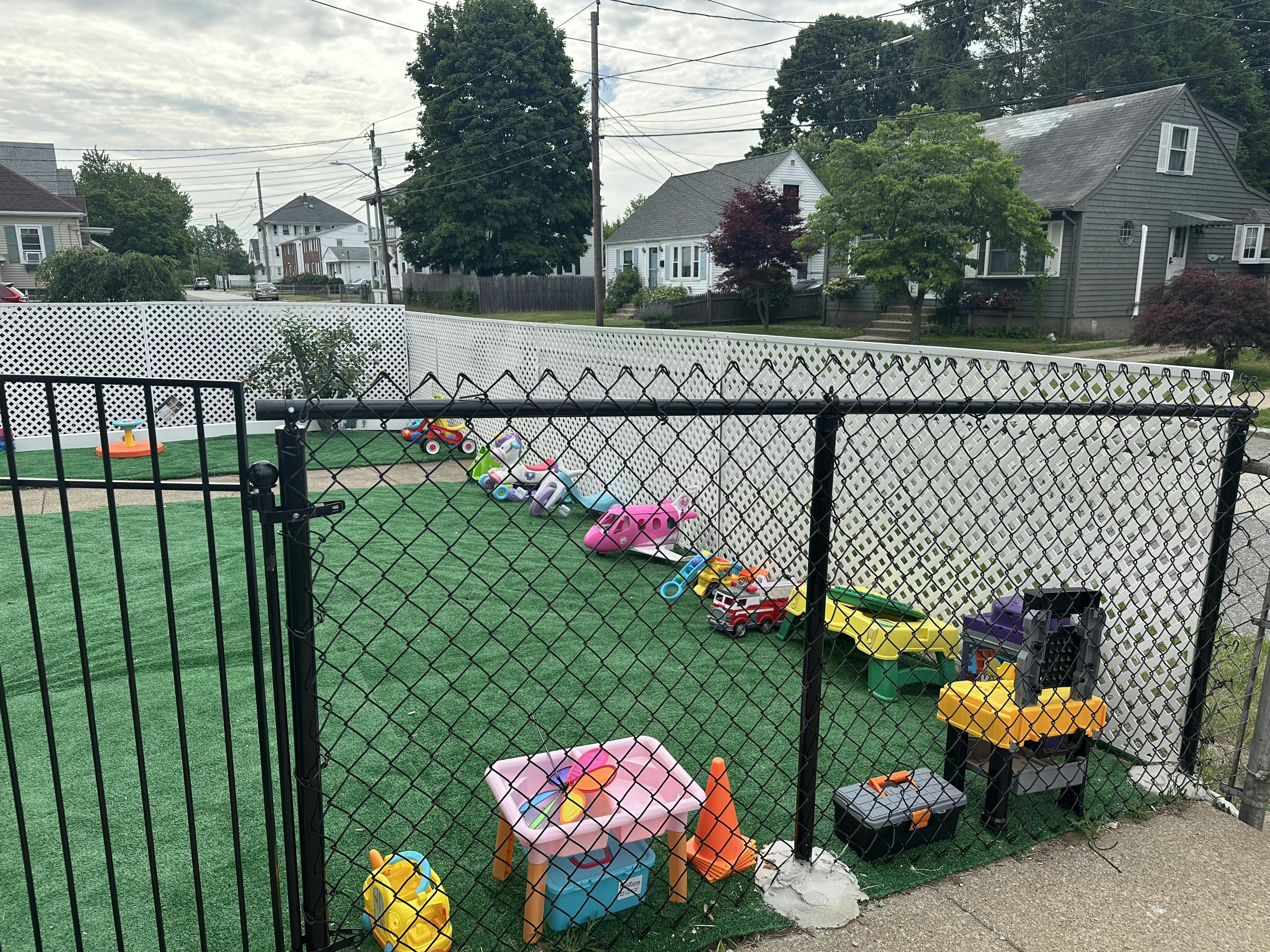Plastic toys scattered on an artificial grass play area behind a chain link fence