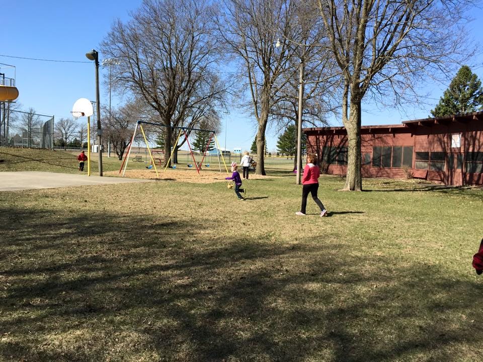 People and a child on a grassy field near a playground