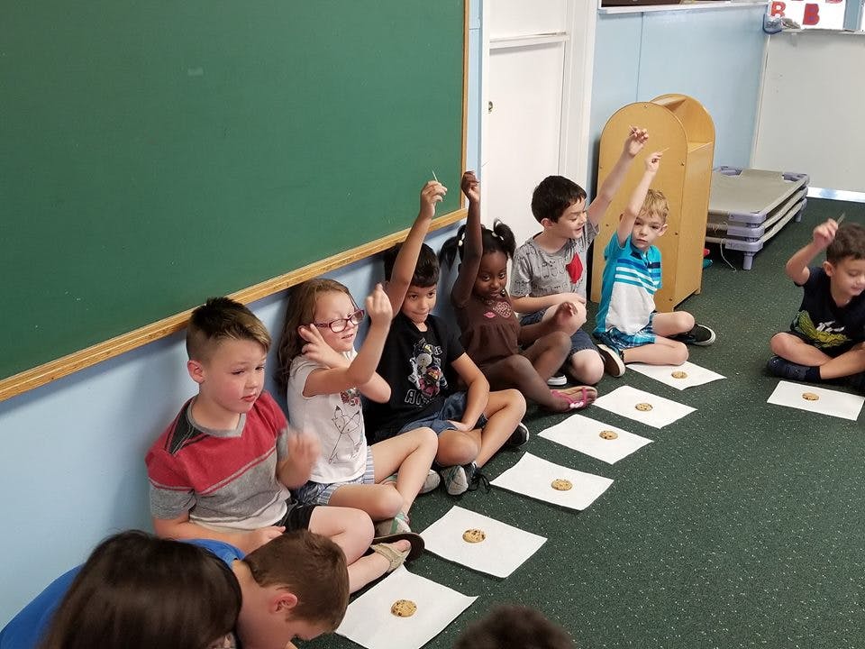 Children sitting on the floor with hands raised in a classroom