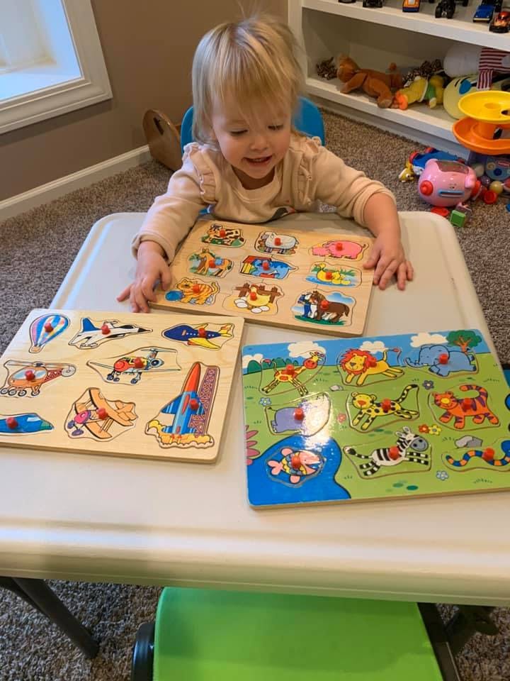 Child playing with three wooden puzzles on a table