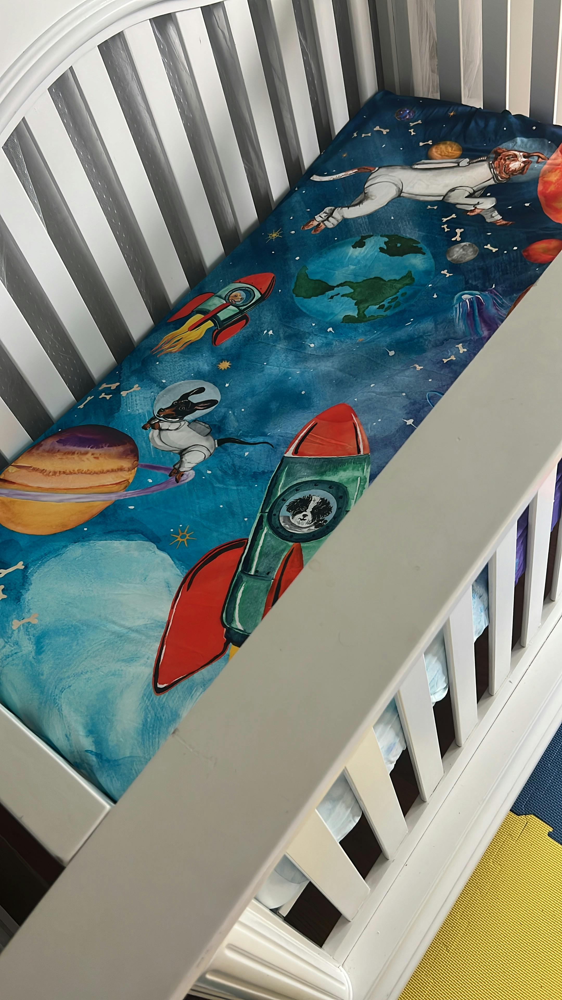 Crib with space-themed bedding featuring rockets and planets