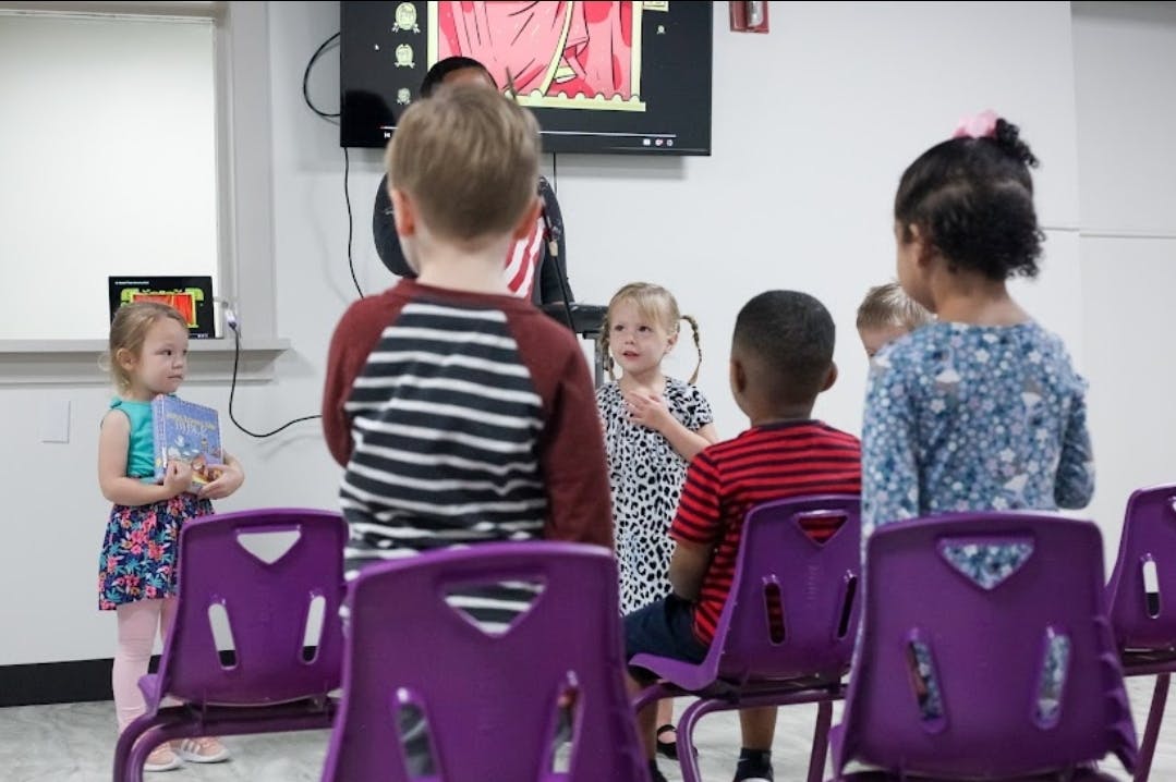 Children in a classroom with some standing and some sitting in chairs