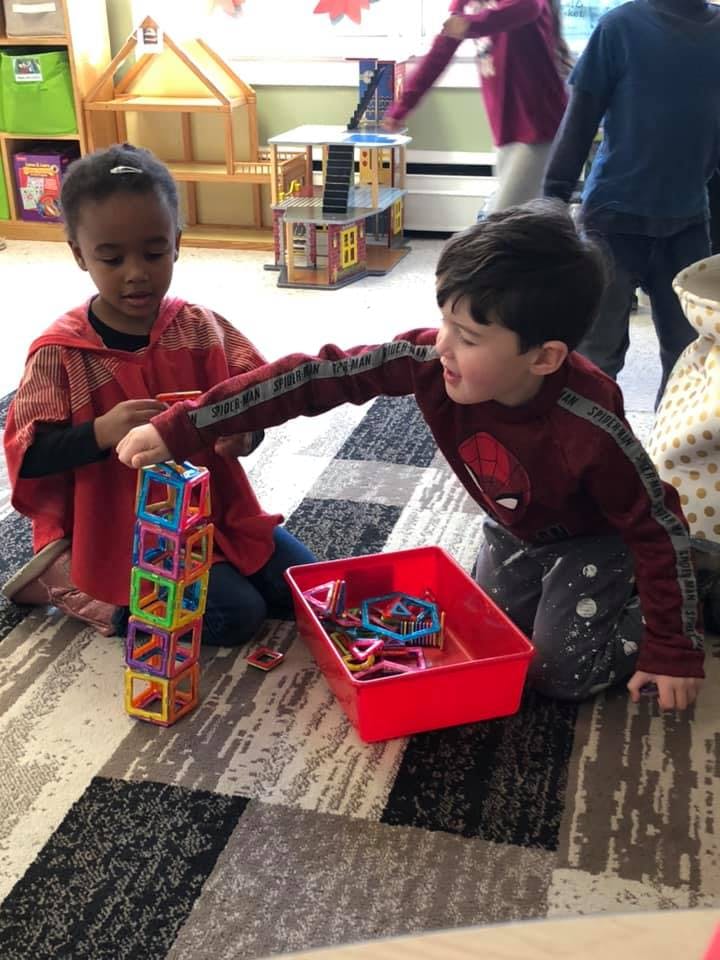 Two children playing with colorful magnetic building blocks on a rug