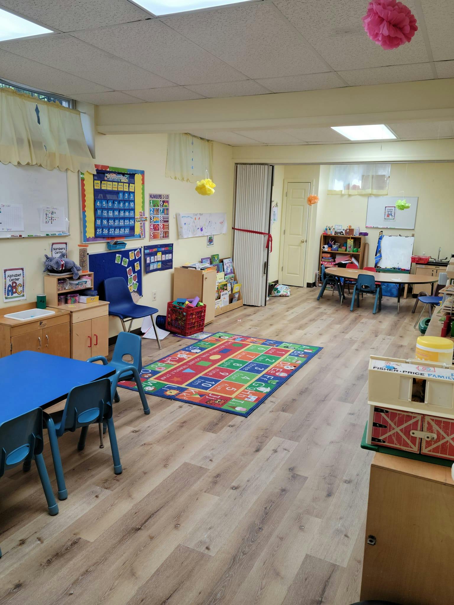 Classroom with small tables and chairs, colorful rug, and learning charts on walls