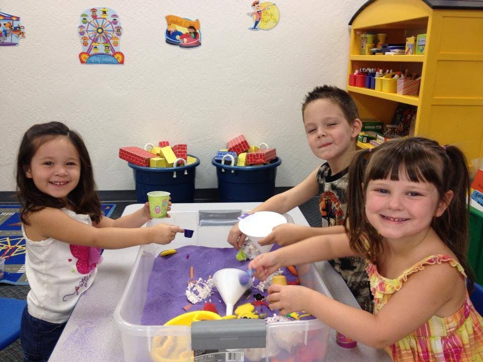 Three children playing with toys in a sensory bin