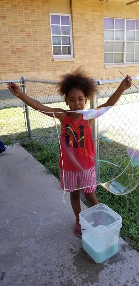 Child making a large bubble with a string and stick tool
