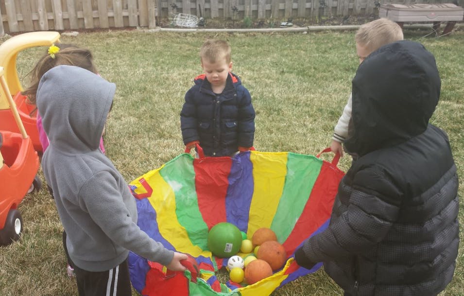 Children playing with a colorful parachute and balls outdoors