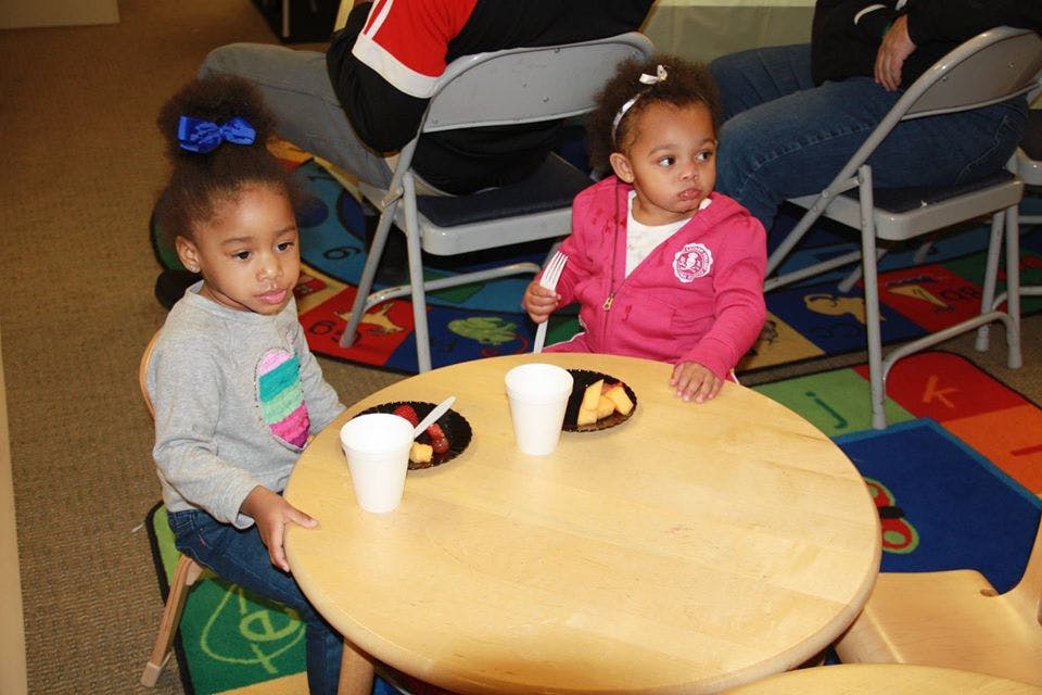 Two children sitting at a small round table with cups and plates