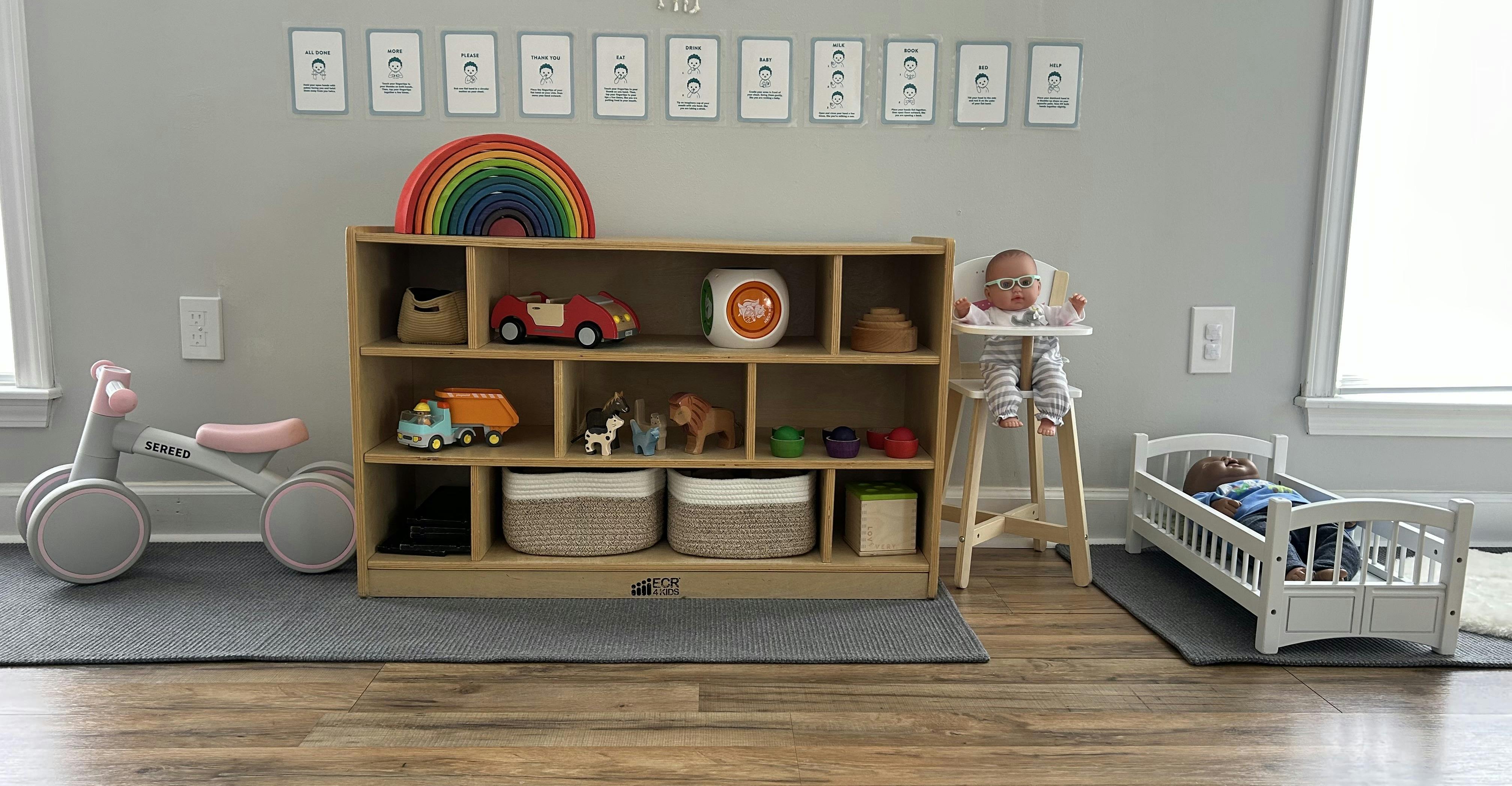 Wooden toy shelf with doll furniture and baby sign language charts on the wall