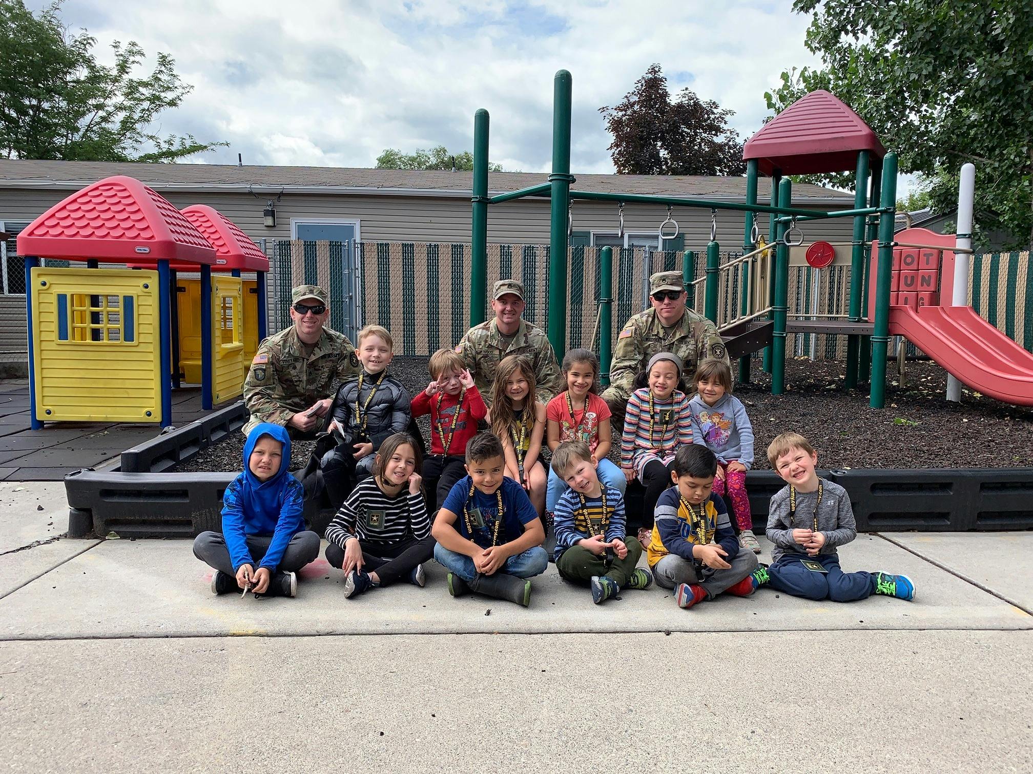Three people in military uniforms with a group of children on a playground