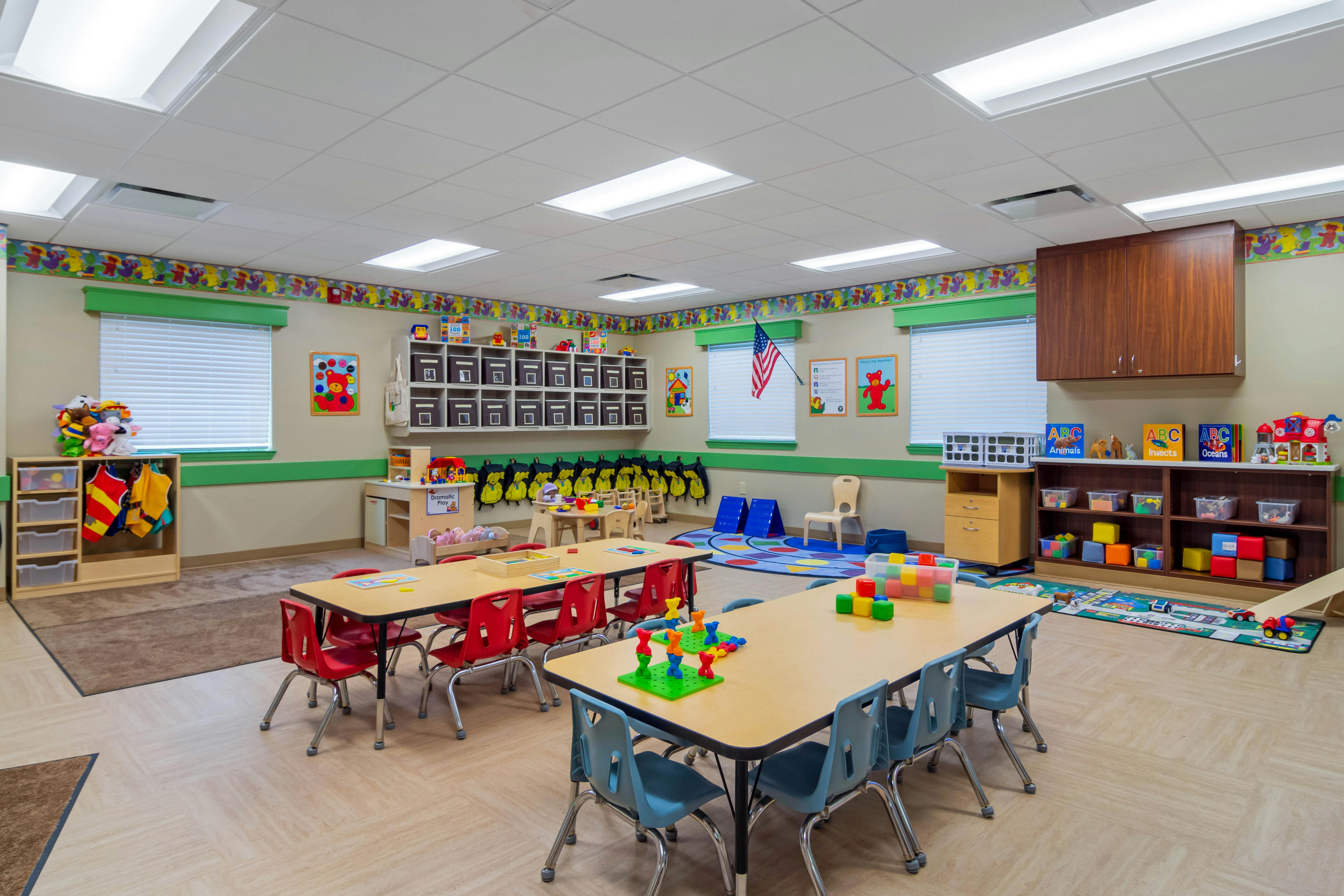 An empty daycare classroom with small tables and chairs arranged for children