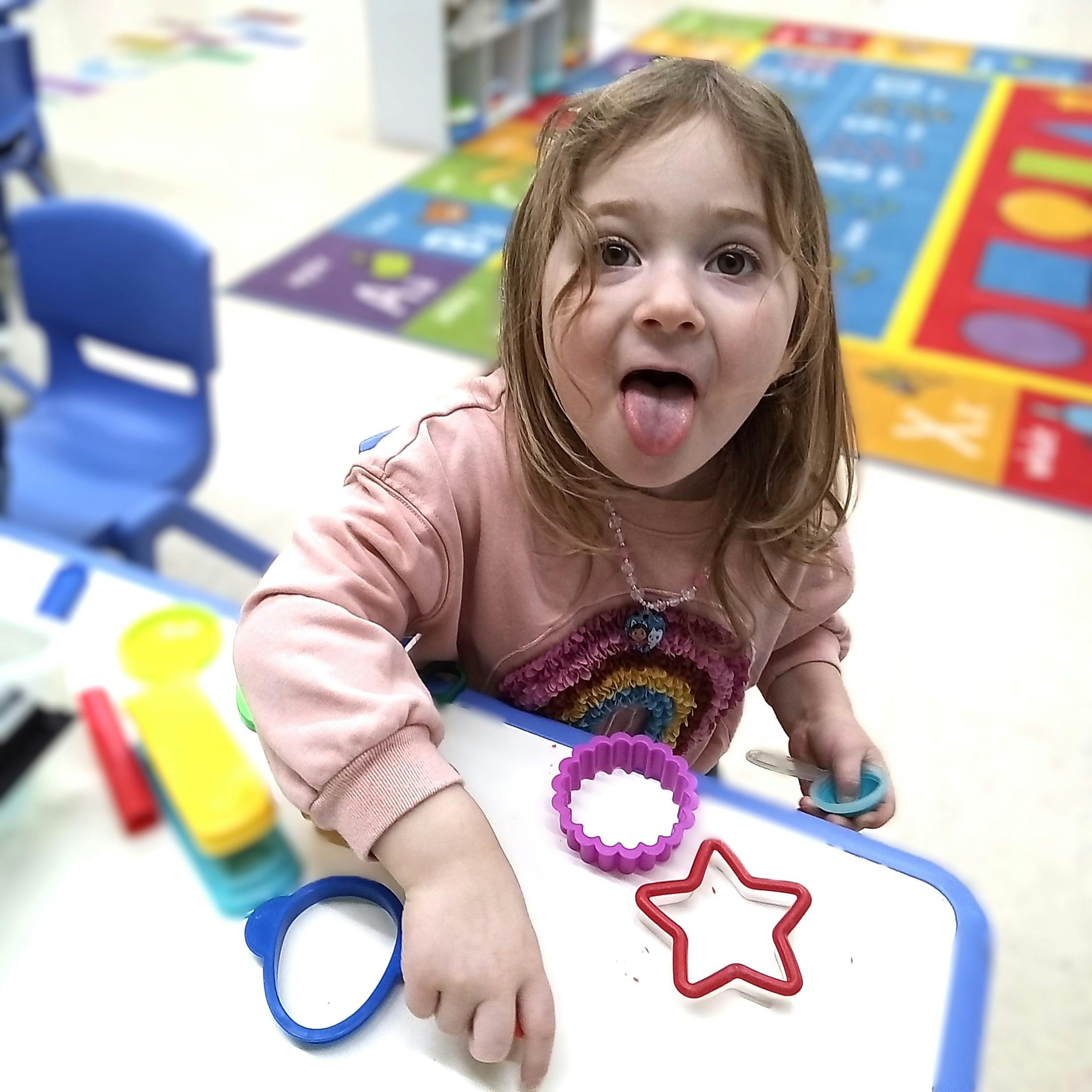 Child sticking out tongue while playing with cookie cutters