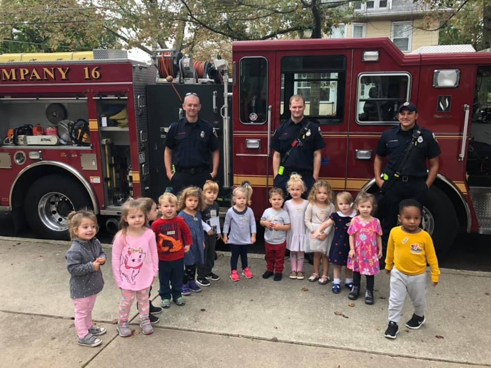 Three people in uniform standing with a group of children in front of a fire truck