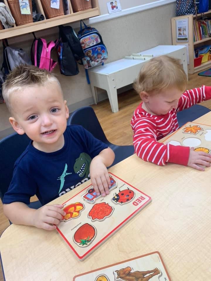 Two children playing with puzzles at a table in a classroom