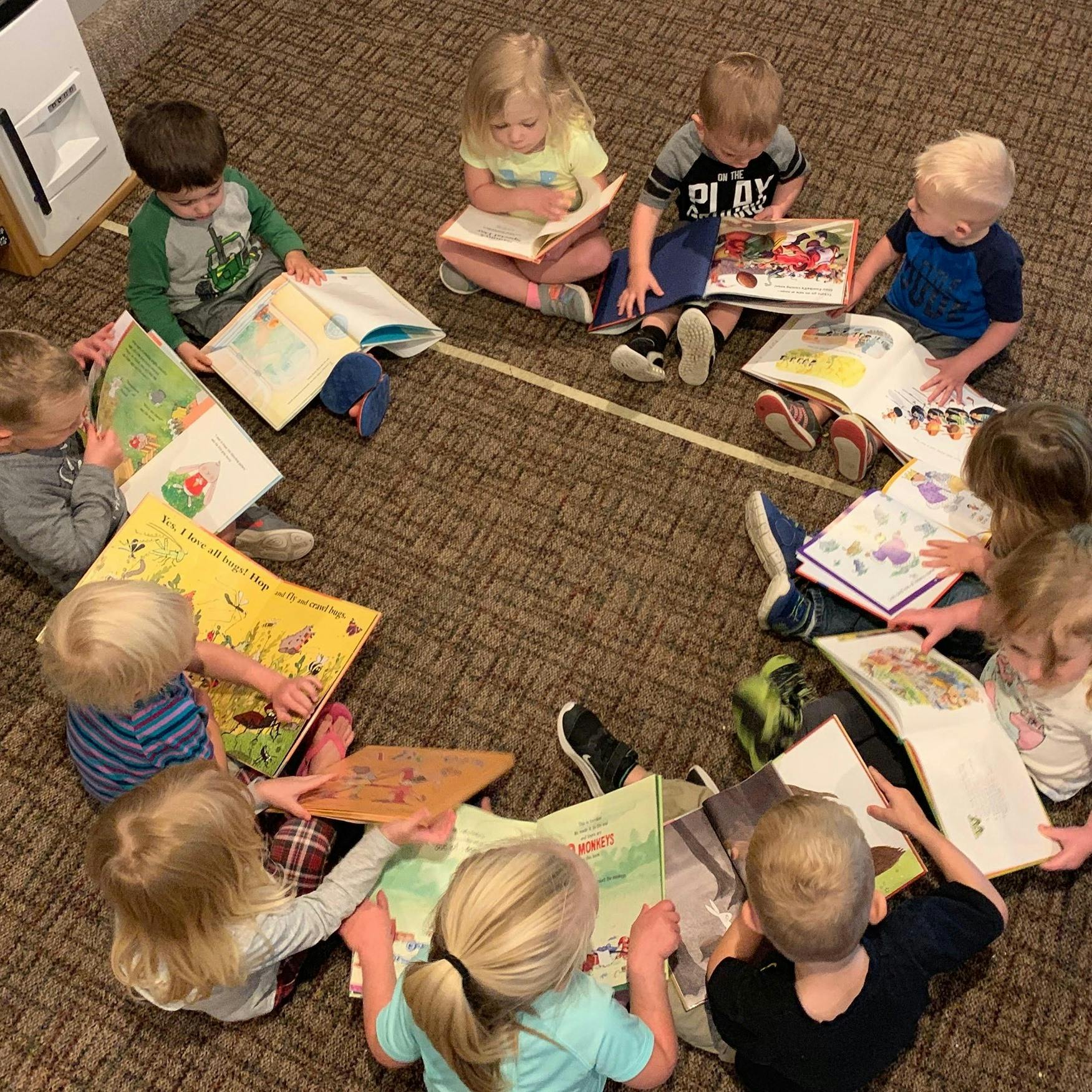 Children sitting in a circle on the floor reading books