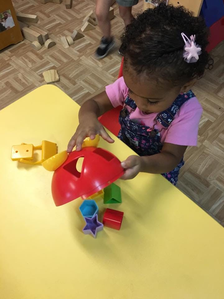 Child playing with a shape sorter toy on a yellow table