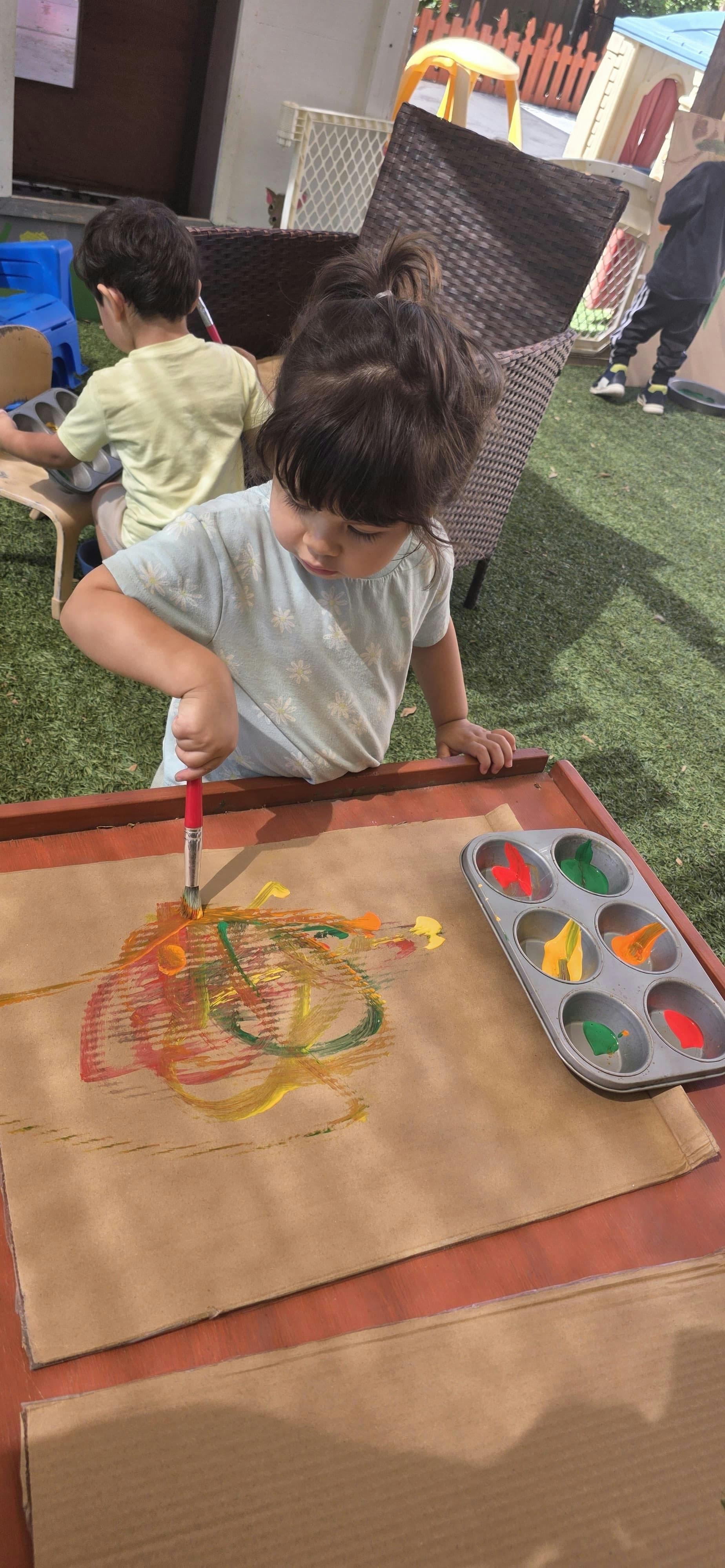 Child painting on cardboard at an outdoor table