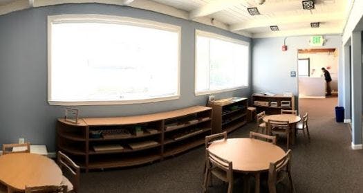 Classroom with small tables and chairs, shelves, and large windows