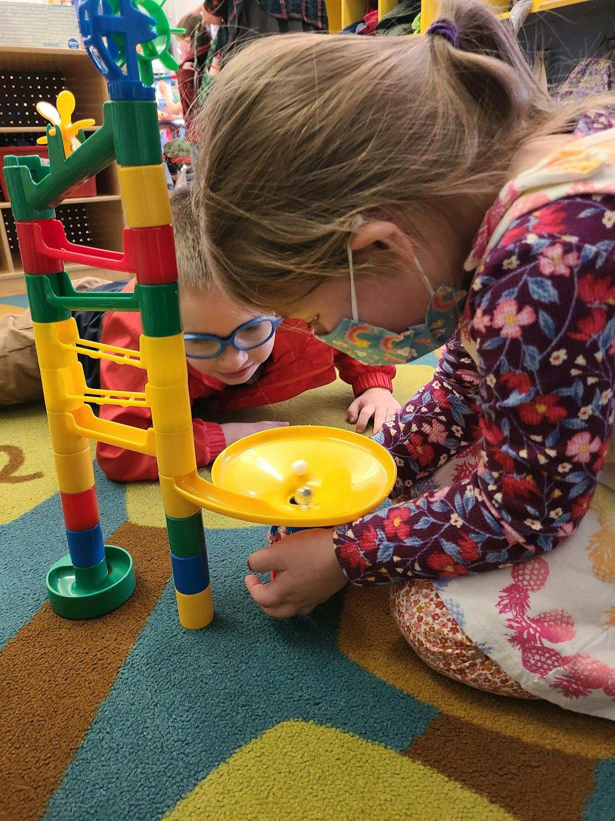 Two children playing with a colorful marble run toy on the floor