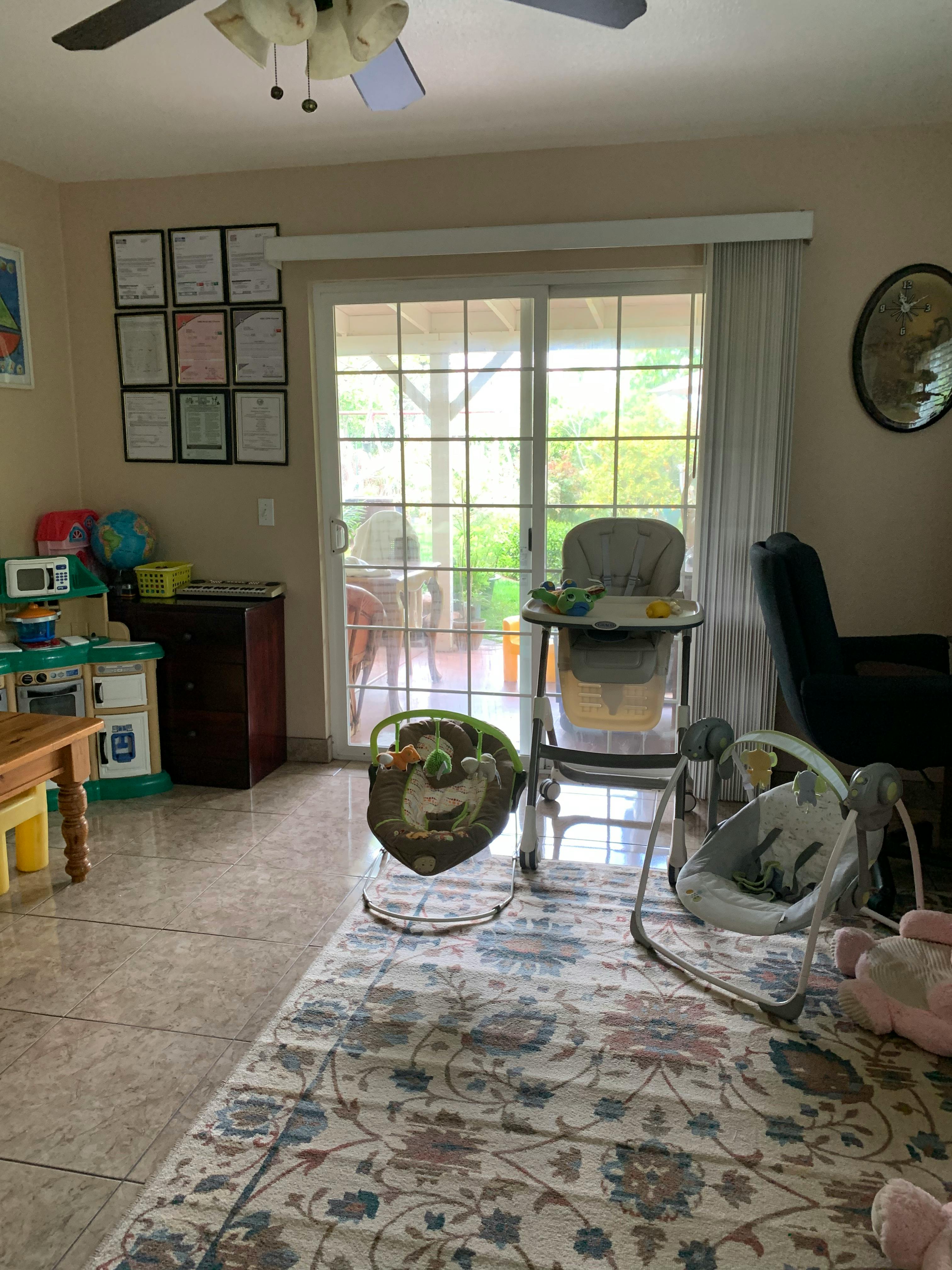 Indoor room with baby high chair, bouncer, and swing near a sliding glass door