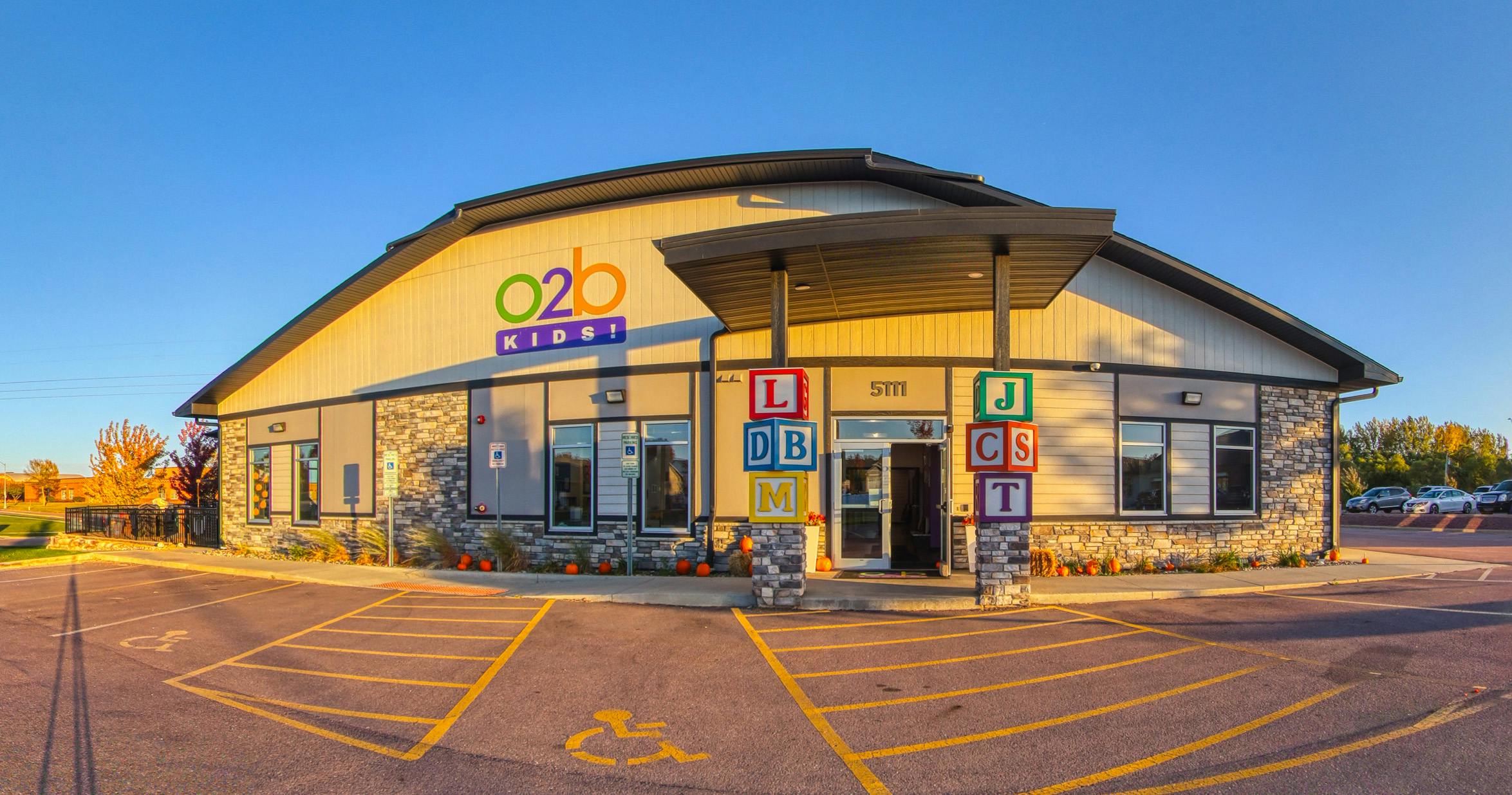 Exterior of a building with a large "O2B Kids!" sign, stone facade, and parking lot