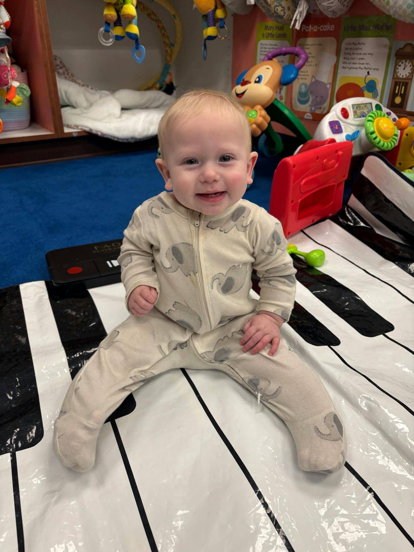 Child in an elephant-patterned onesie sitting on a floor piano mat